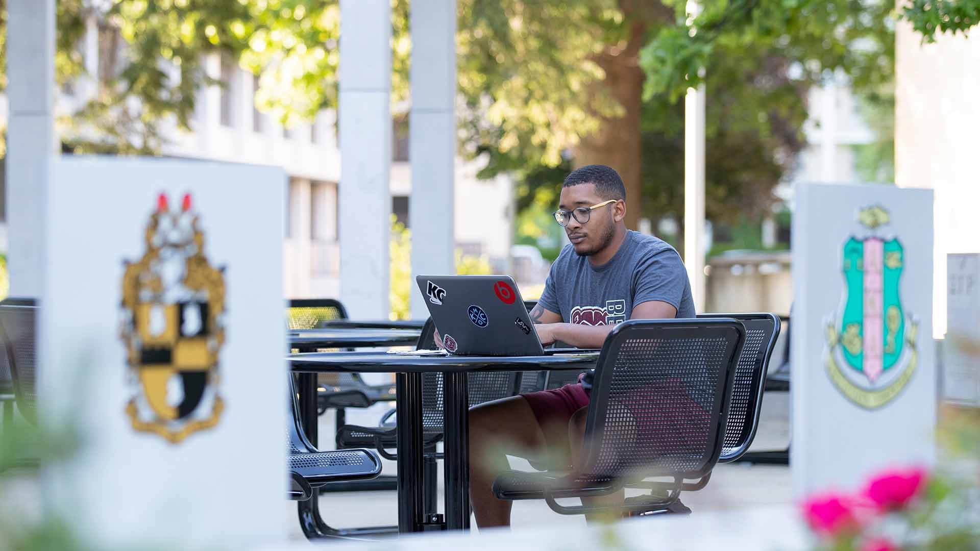A student using his laptop while sitting in a campus courtyard.